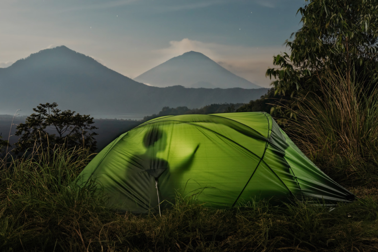 Silhouette of person in tent looking at device, mountains in the background